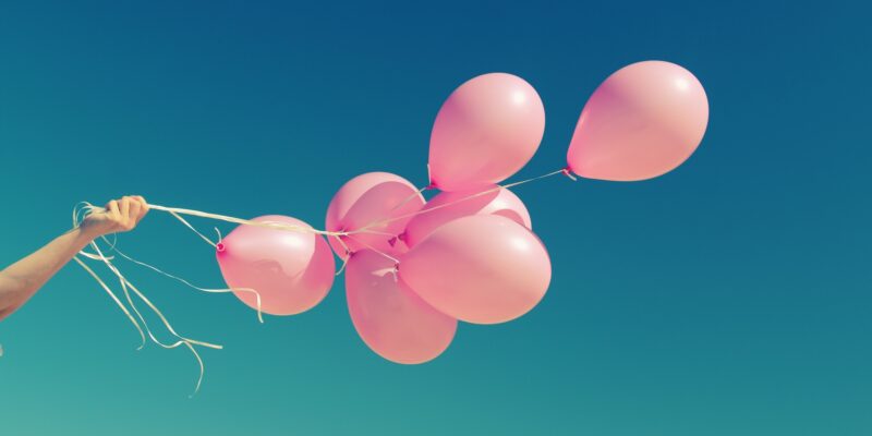 한 여성이 7개의 핑크색 풍선에 끈을 매달아 한 손으로 풍선 다발을 쥐고 있다.
